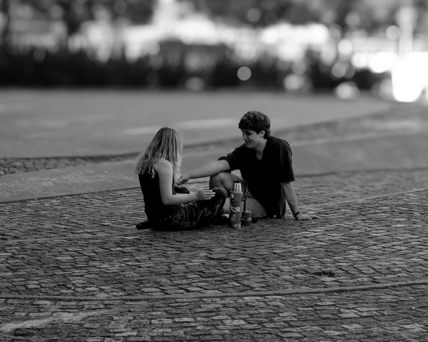 A young couple sitting and chatting on a cobblestone street, enjoying leisure time.