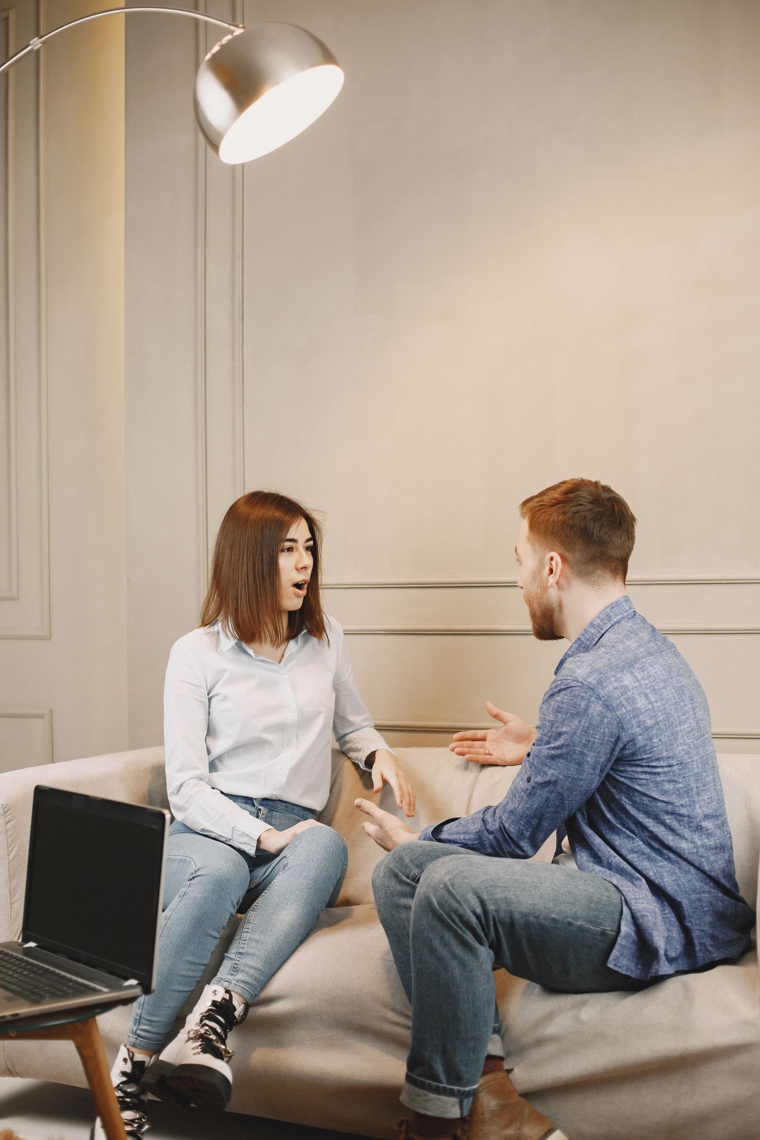 A young couple having a serious conversation on a couch in a modern living room setting.