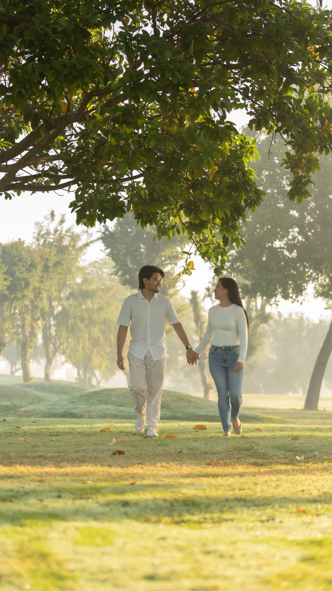Couple walking hand-in-hand in a misty park.