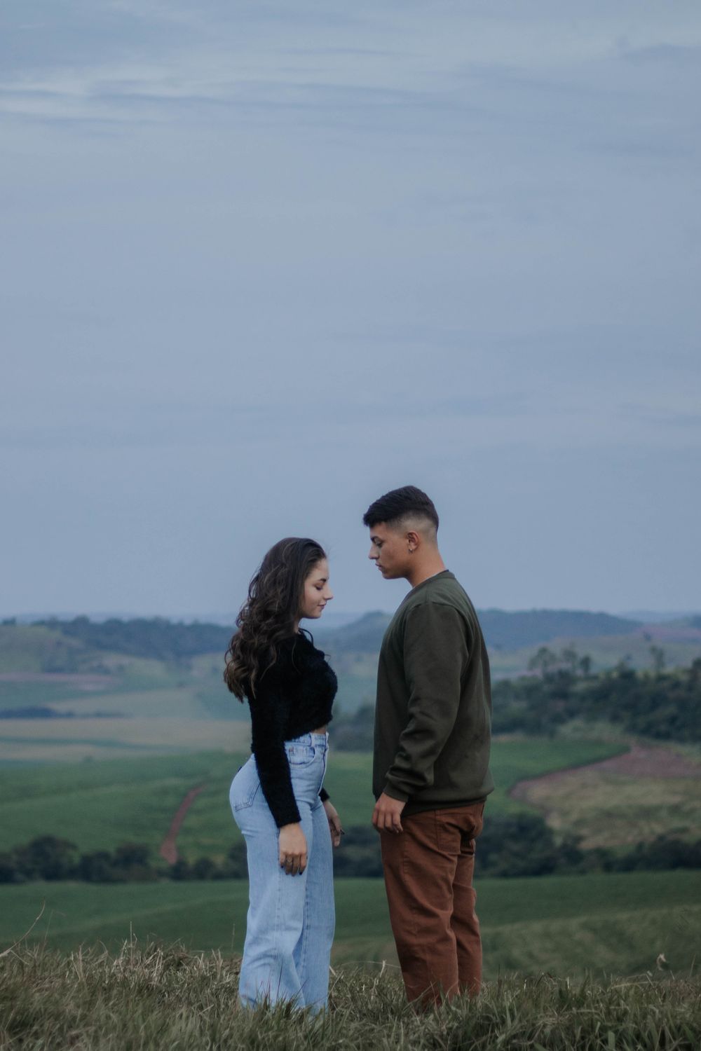 Young couple standing in a serene grassland setting, surrounded by expansive countryside views.