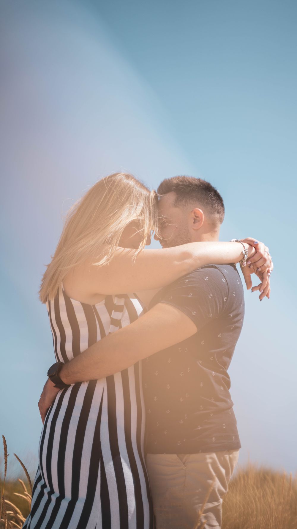 A loving couple embracing outdoors under a clear blue sky, capturing romance and connection.