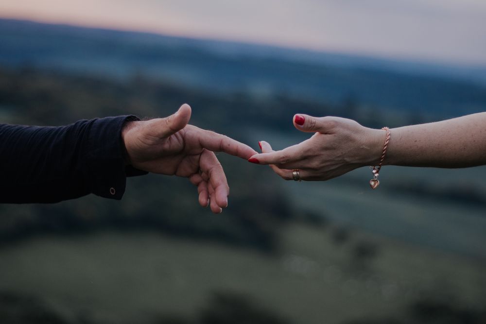 A romantic moment with hands reaching out in a peaceful outdoor setting captured at twilight.