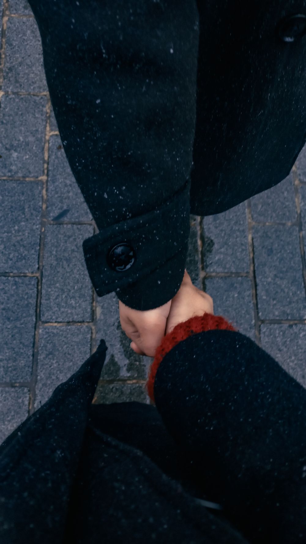 A close-up of a couple holding hands on a snowy pavement in Istanbul, Türkiye, during winter.