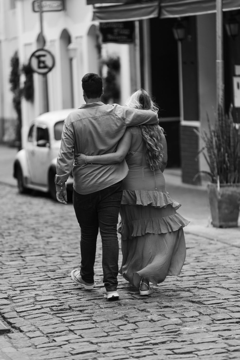 A back view of a couple strolling arm-in-arm down a cobblestone street, captured in a stylish black and white photo.