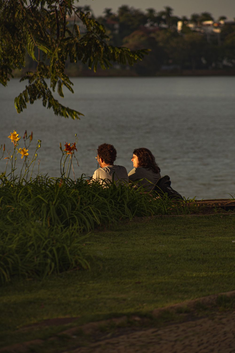 A serene scene of a couple sitting by the lake with flowers and evening light casting warm tones.