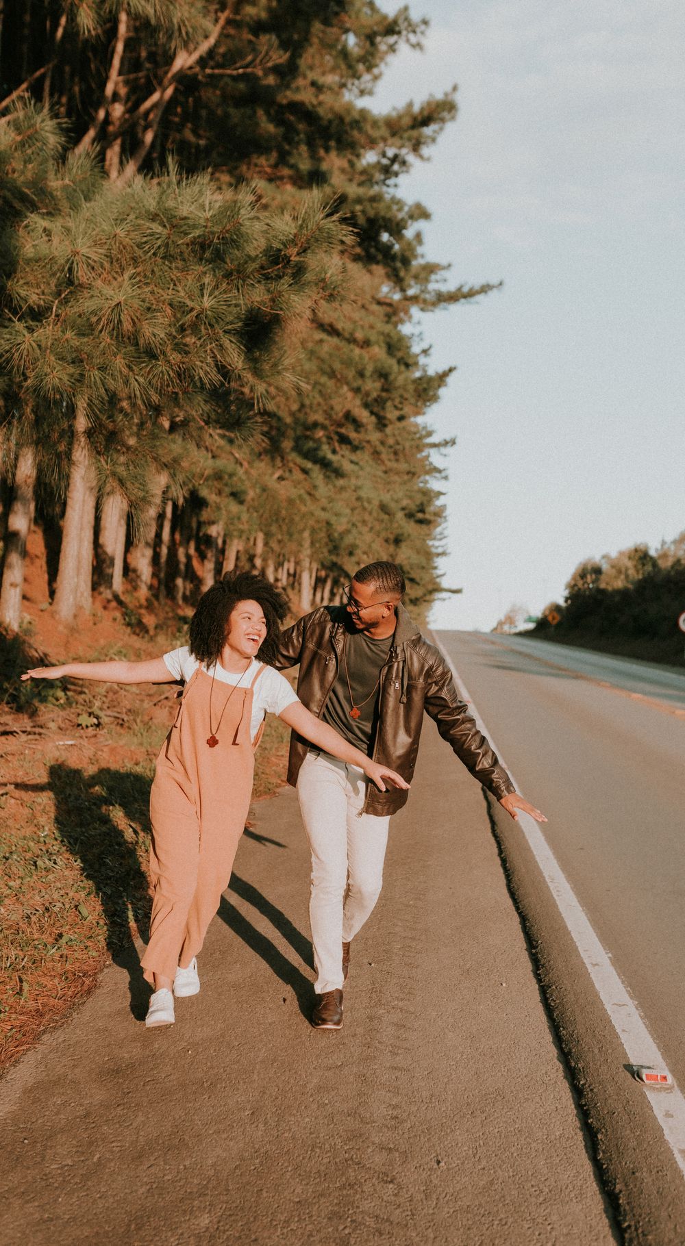 A joyful couple walks along a scenic rural road, arms stretched wide, under the summer sun.