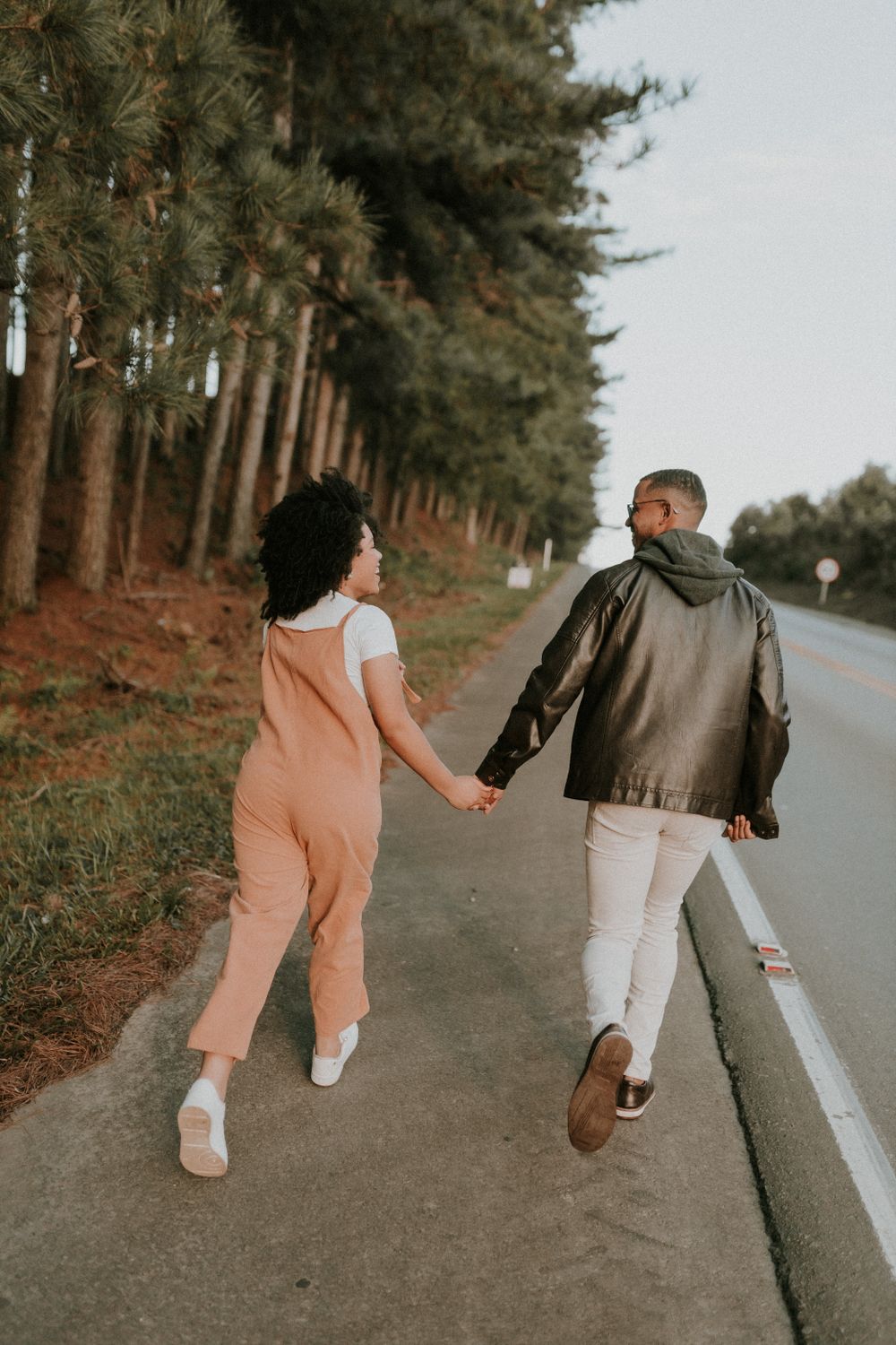 A couple walks hand in hand along a road beside a forest, symbolizing love and togetherness.