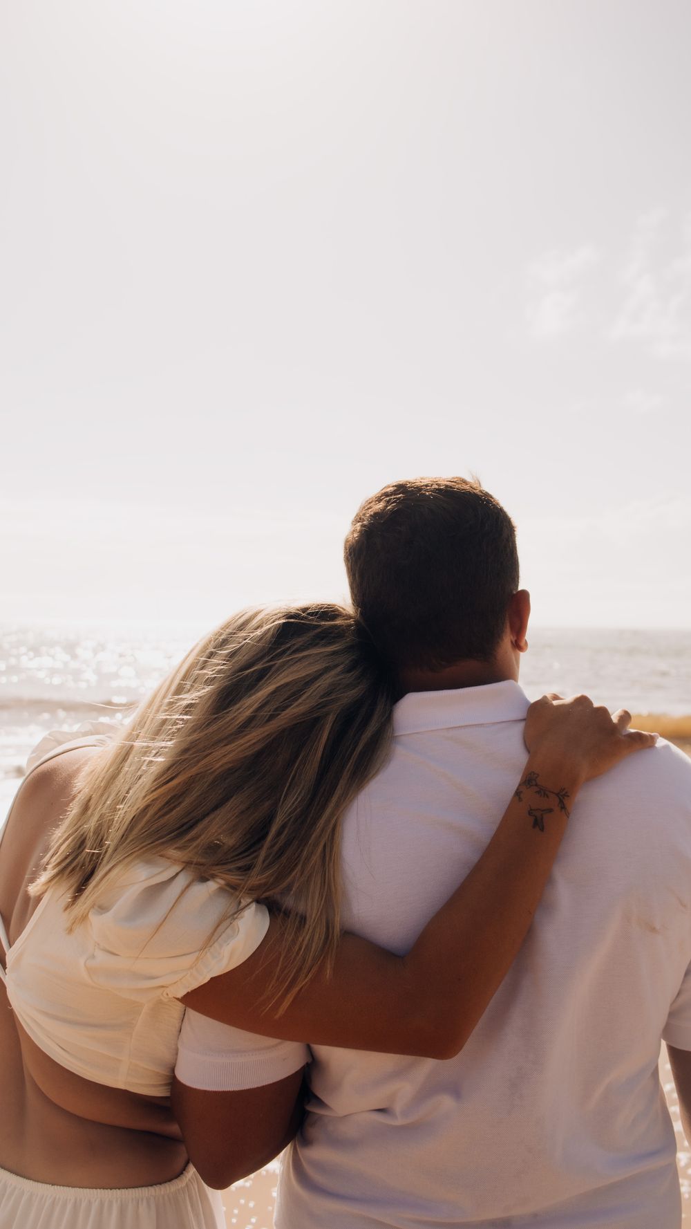 Romantic couple in warm embrace on a sunny beach, looking at the sea. Perfect for love and travel themes.