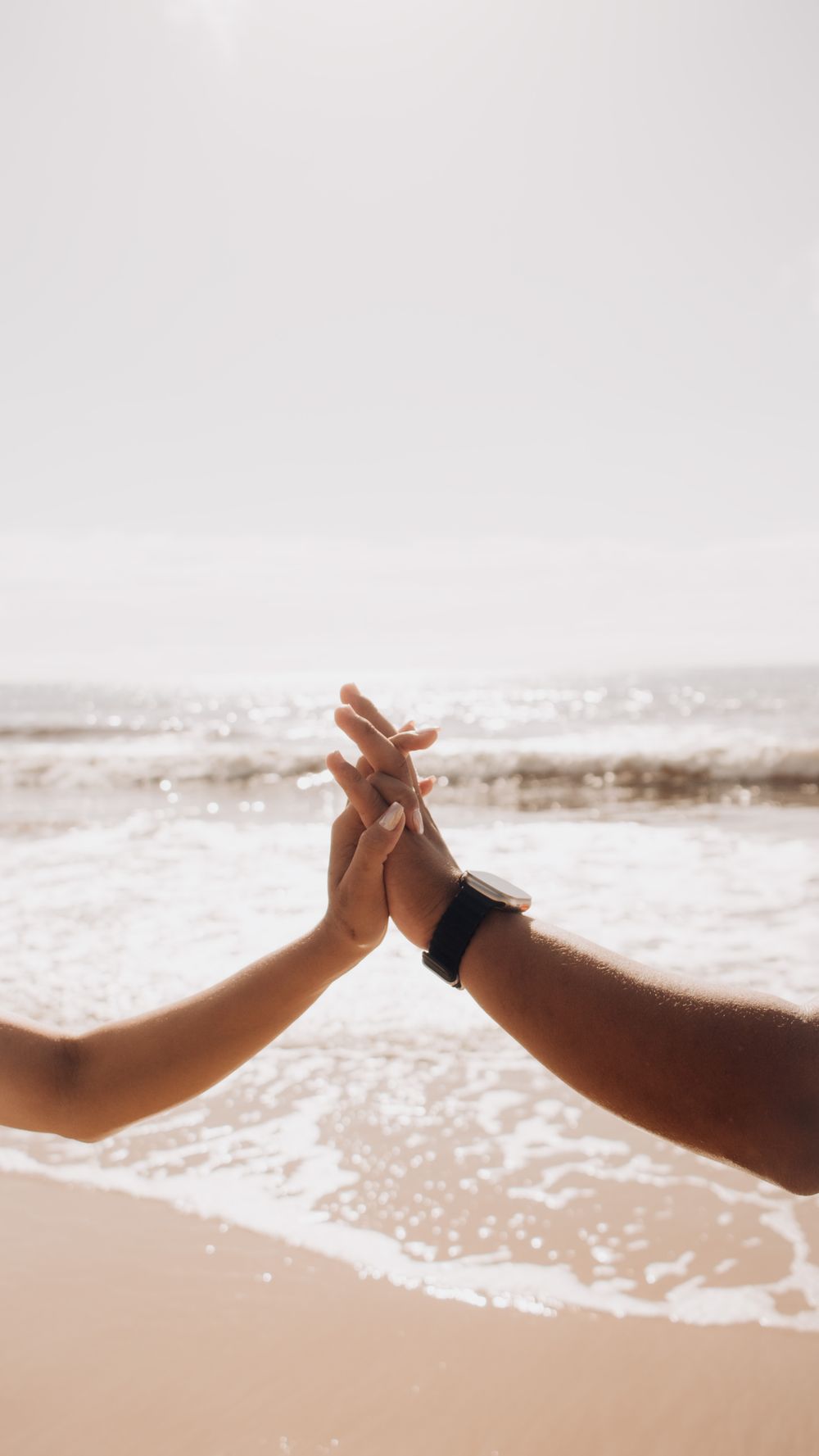 Silhouettes of a couple holding hands by the sea on a bright sunny day, symbolizing love.