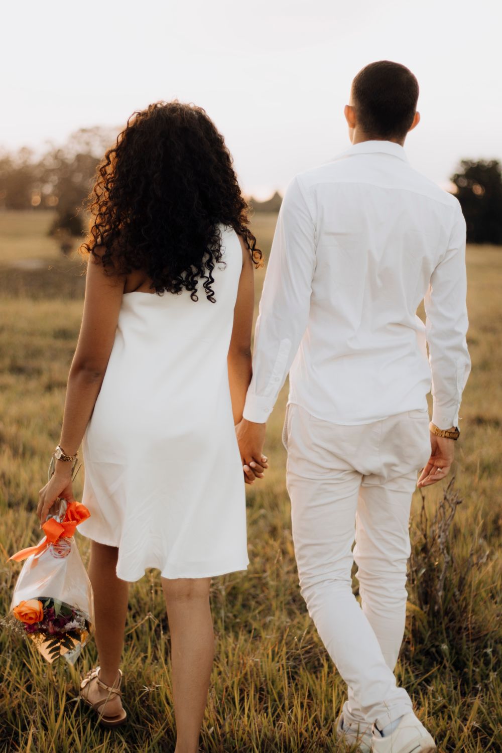 A couple walking hand in hand through a grassy field at sunset, romantic and serene.