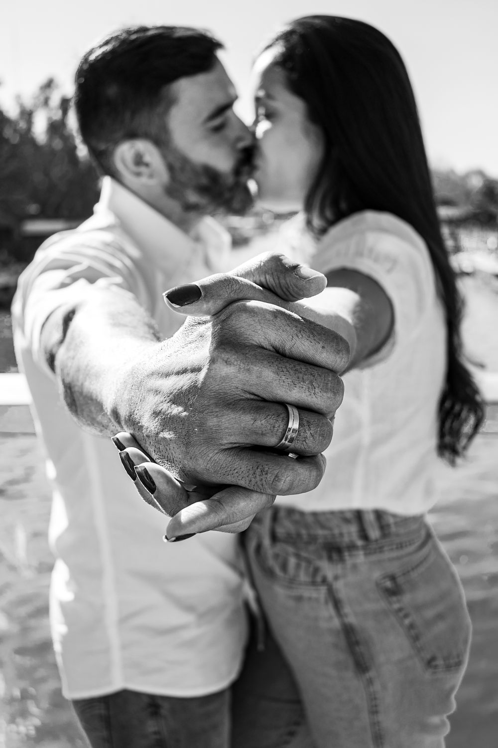 A black and white photo capturing a romantic couple holding hands with a blurred kiss in the background.