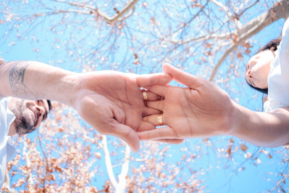 A tender moment between a couple holding hands under a bright blue sky with autumn leaves.