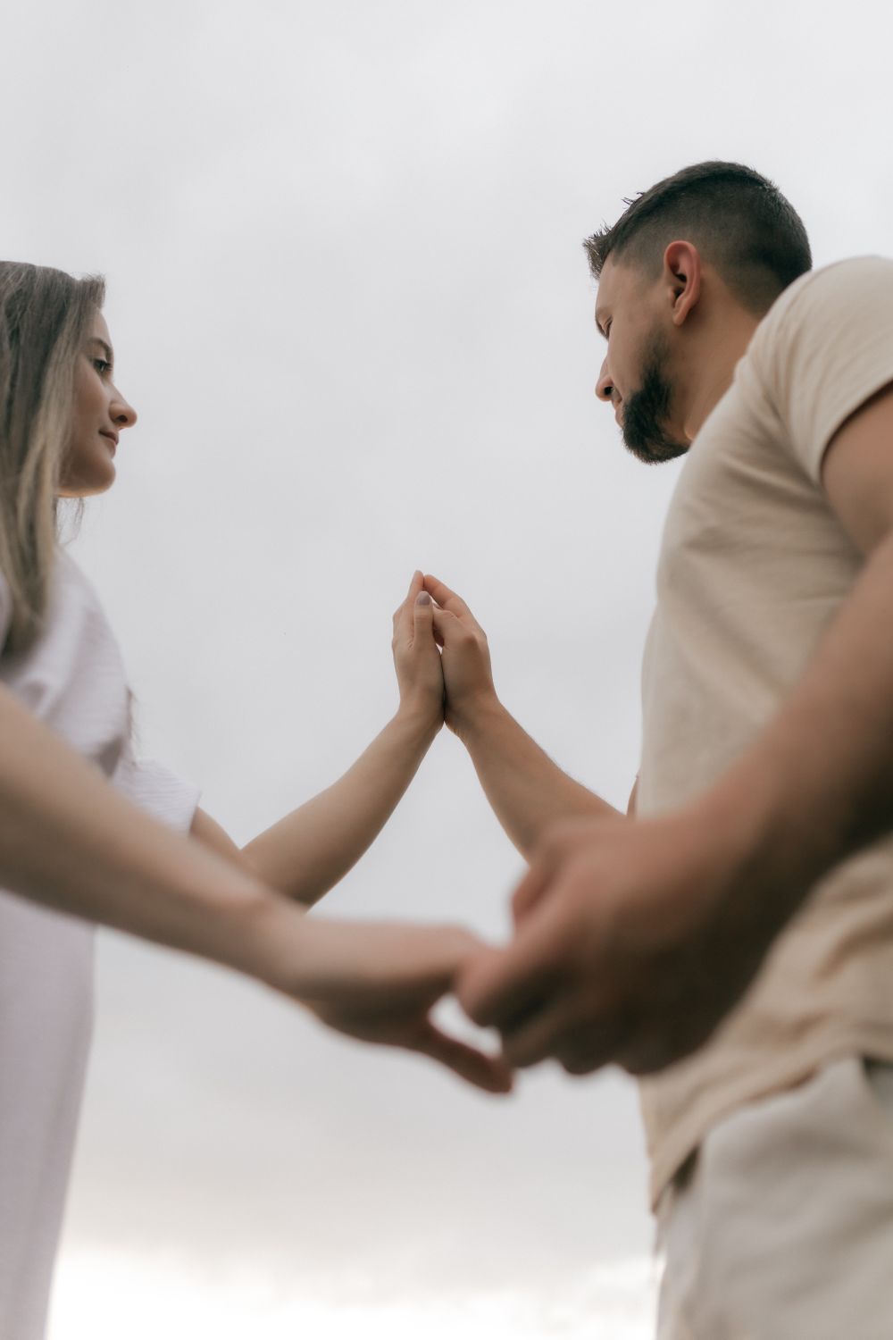 A couple connecting and holding hands against a cloudy sky, symbolizing love and unity.