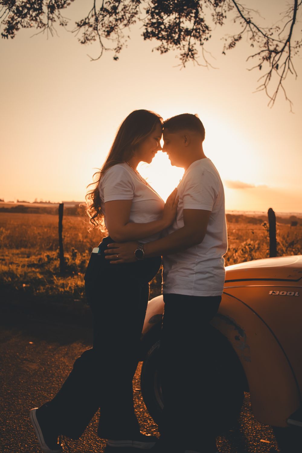 A loving couple embraces by a car during a beautiful sunset, creating a warm, romantic scene.
