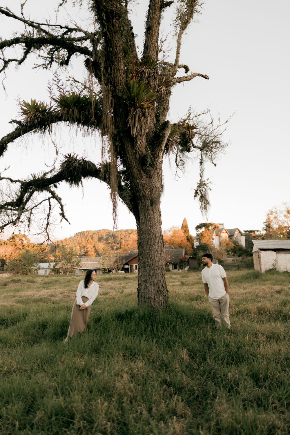Two adults stand beneath an ancient tree in a scenic countryside, enjoying a peaceful moment.