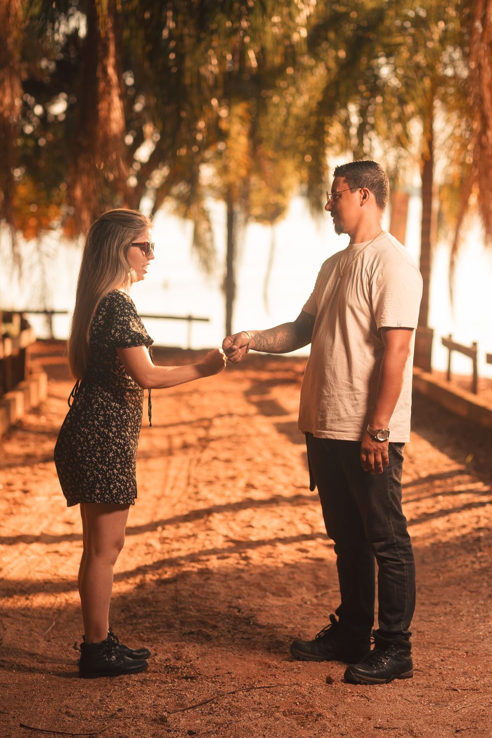 A couple shares a friendly fist bump in a sunlit outdoor setting with trees.