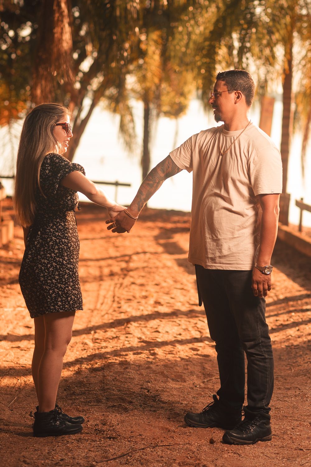 A couple stands holding hands under palm trees in warm sunlight, creating a romantic atmosphere.