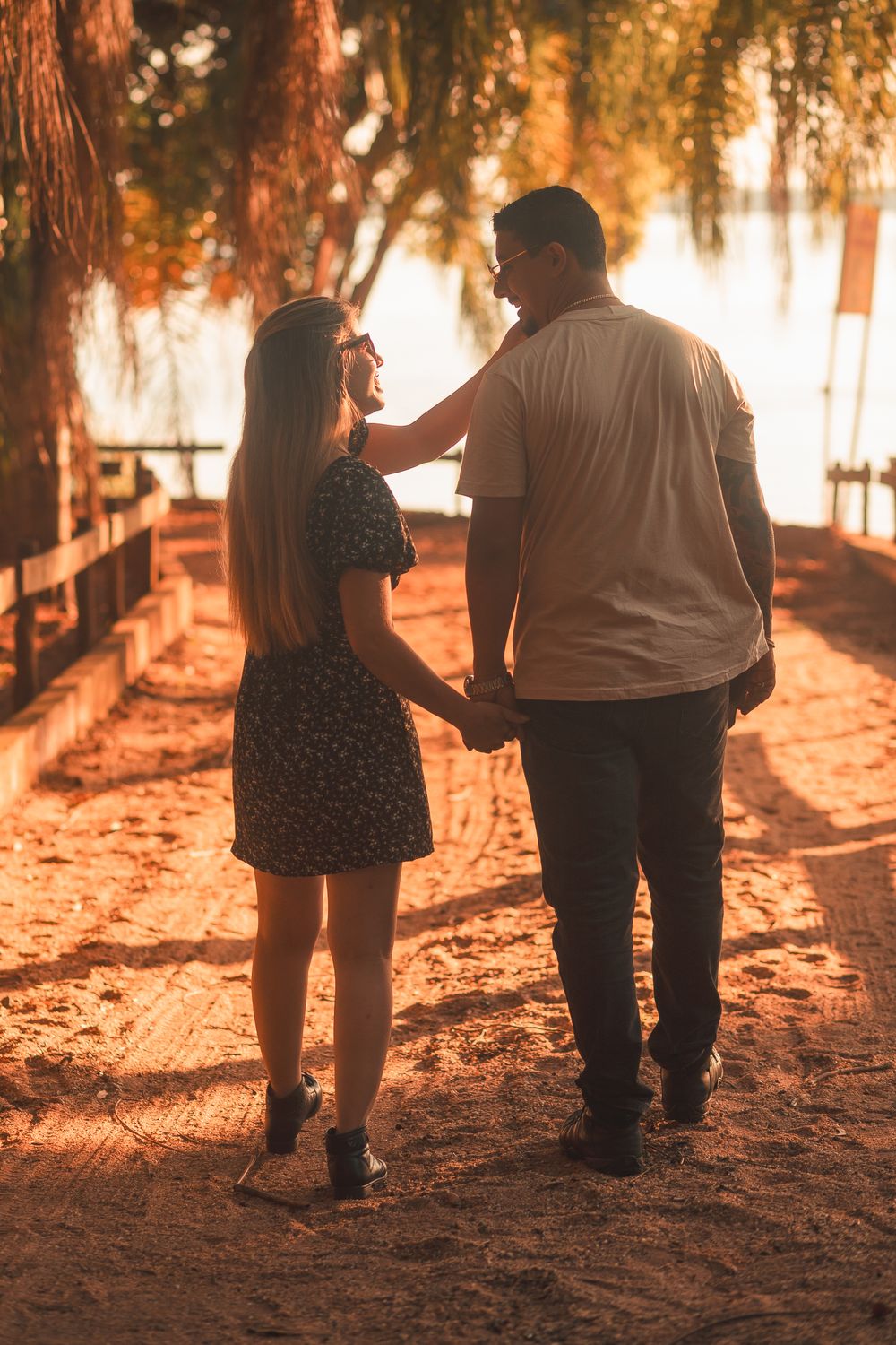 A couple holding hands during a romantic walk at sunset on a sunlit pathway.