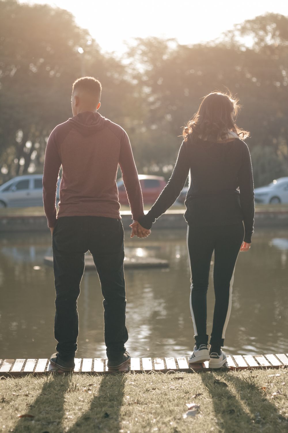 A couple stands hand in hand by a serene lake at sunset, creating a romantic and peaceful scene.