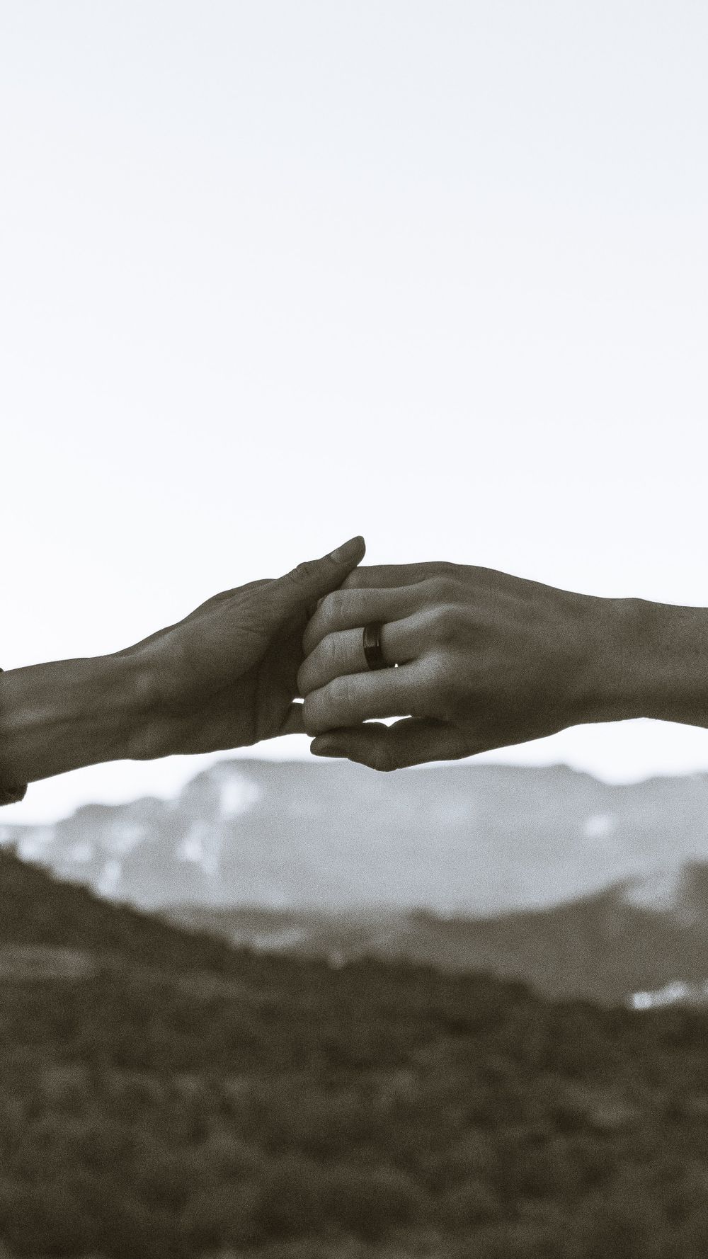 Two hands gently holding with a scenic mountain backdrop, symbolizing love and connection.