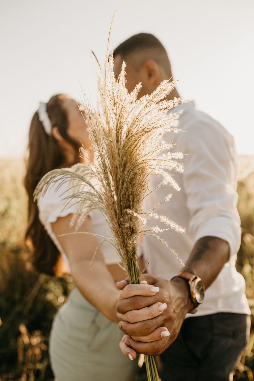 Side view of multiethnic couple standing close and hiding behind bunch of grass in rural field in sunny day